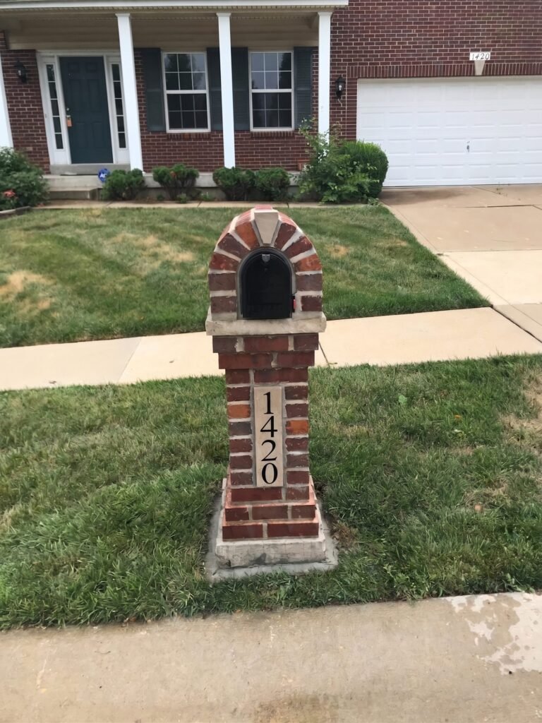 Arched brick mailbox with stone keystone cap and stone address plaque, near a two-car garage