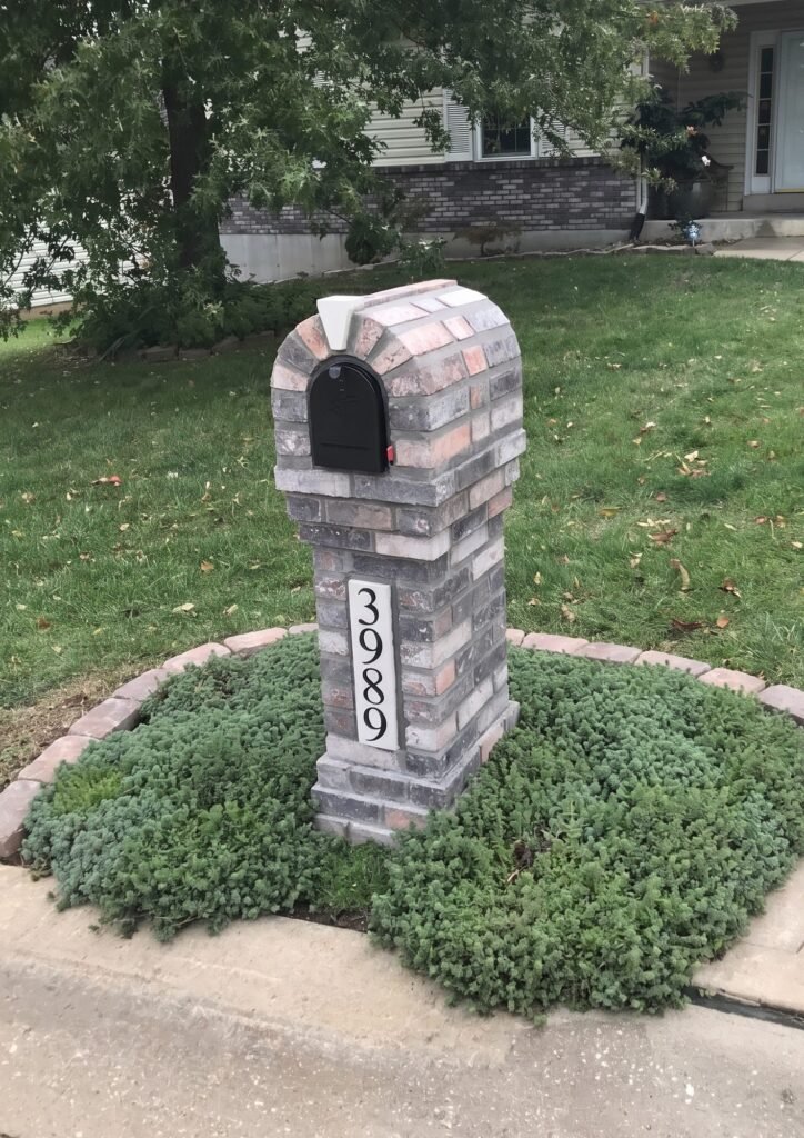 Round-topped brick mailbox in blended gray and rust brick, set in a circular groundcover bed