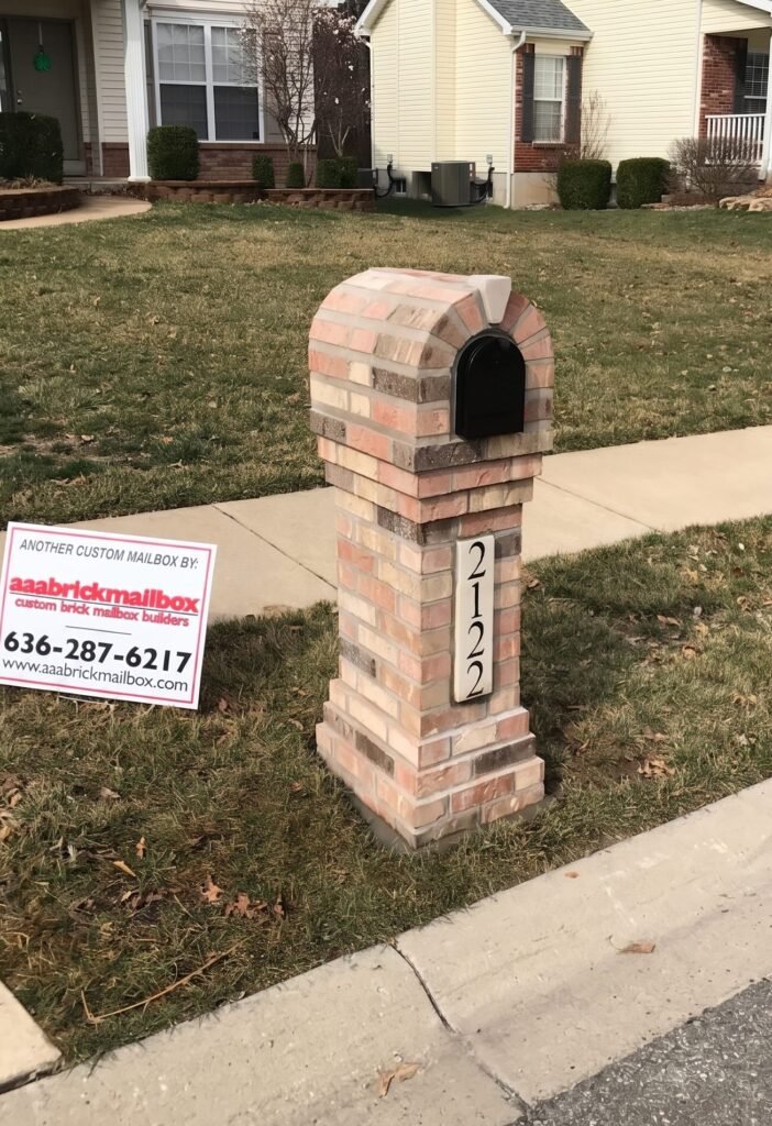 Arched tan and gray brick mailbox on a paver base, set curbside beside the sidewalk