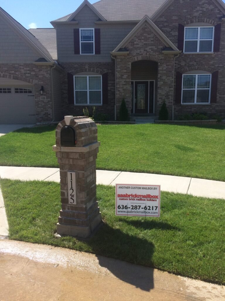 Arched brick mailbox on a tapered stone base, fresh lawn and a two-story brick house behind
