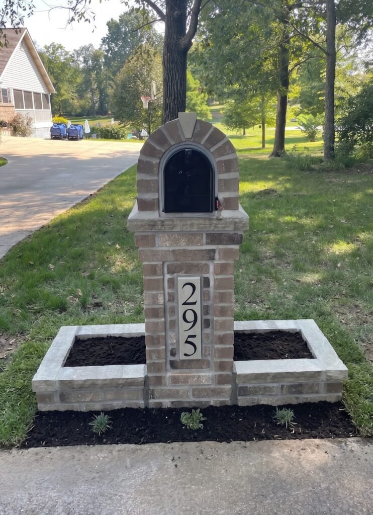 Arched brick mailbox flanked by two brick planter boxes filled with soil, pine tree overhead