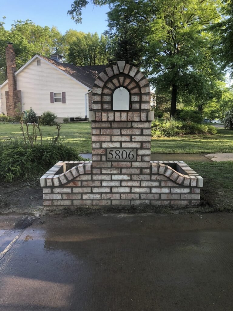 Whitewashed brick mailbox viewed head-on, showing the arched mailbox door and matching planter walls