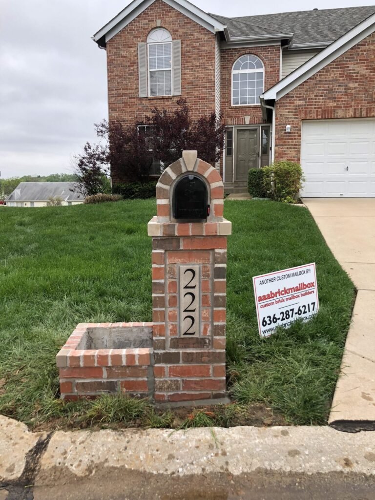 Arched brick mailbox with a single brick planter box, two-story brick house with dormer windows behind