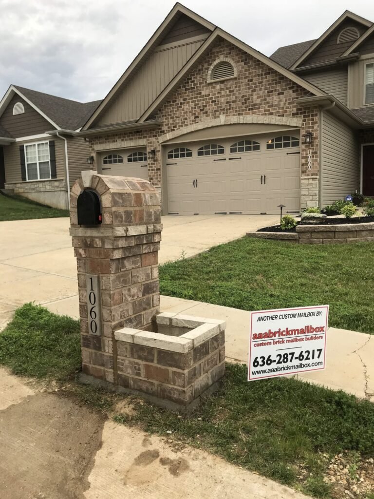 Arched tan brick mailbox with a single brick planter box, matching tan two-car garage behind