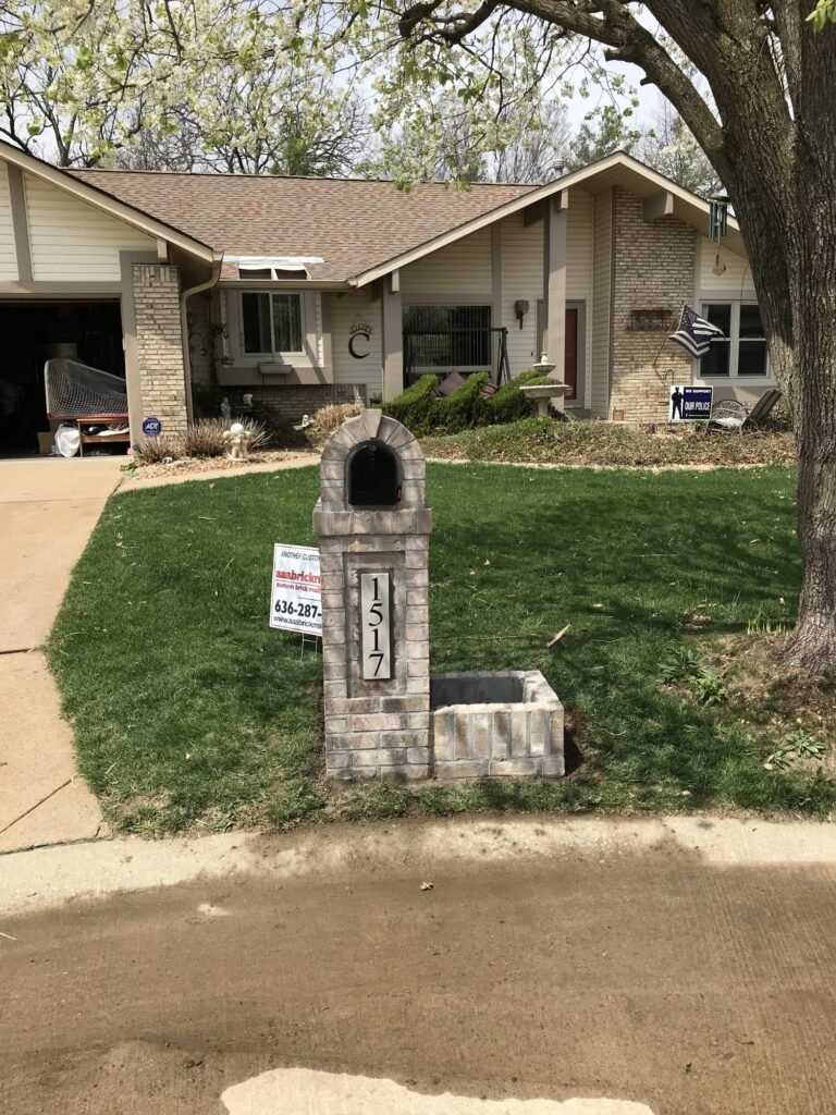 Arched brick mailbox with a single brick planter box, same flowering tree overhead as the previous photo