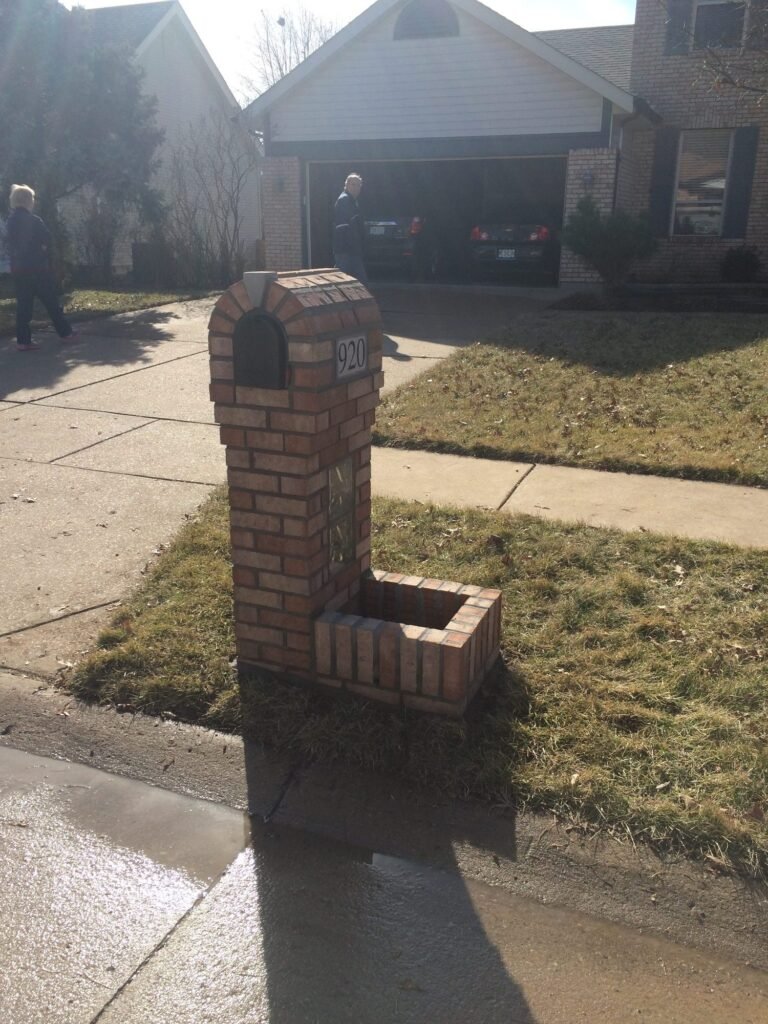 Arched red brick mailbox with a white mailbox door and a glass block accent window, garage visible behind