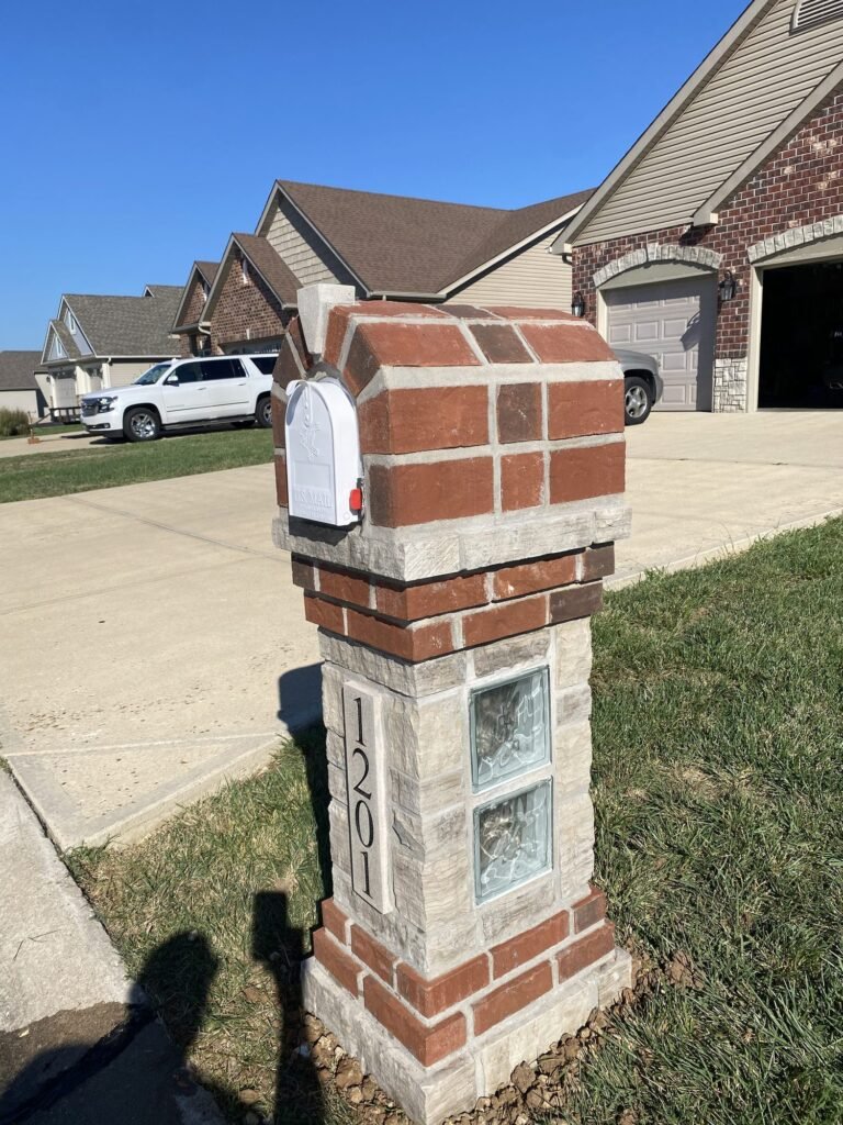 Arched red brick mailbox with a white mailbox door and two glass block accent windows on a stone-capped column