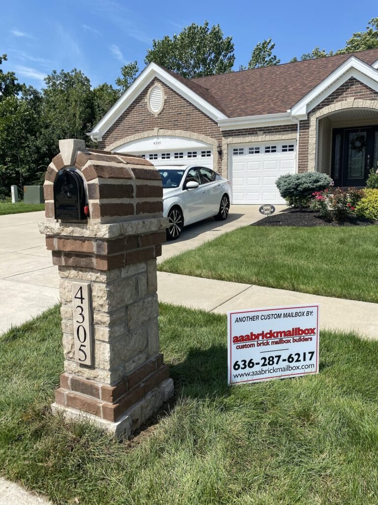 Arched red brick dome top with tan stone shoulders on a stacked cream stone pillar, number plaque below, beside a driveway