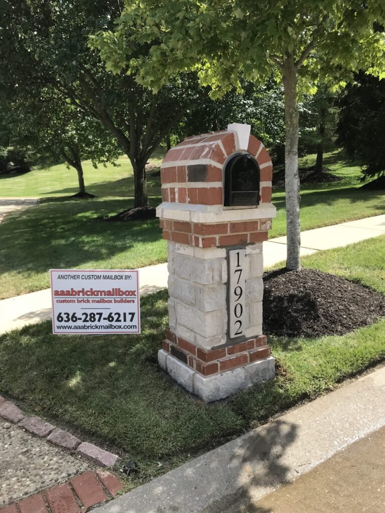 Red brick arched dome top on a stacked stone pillar, shaded by a tall maple tree, number plaque near the sidewalk