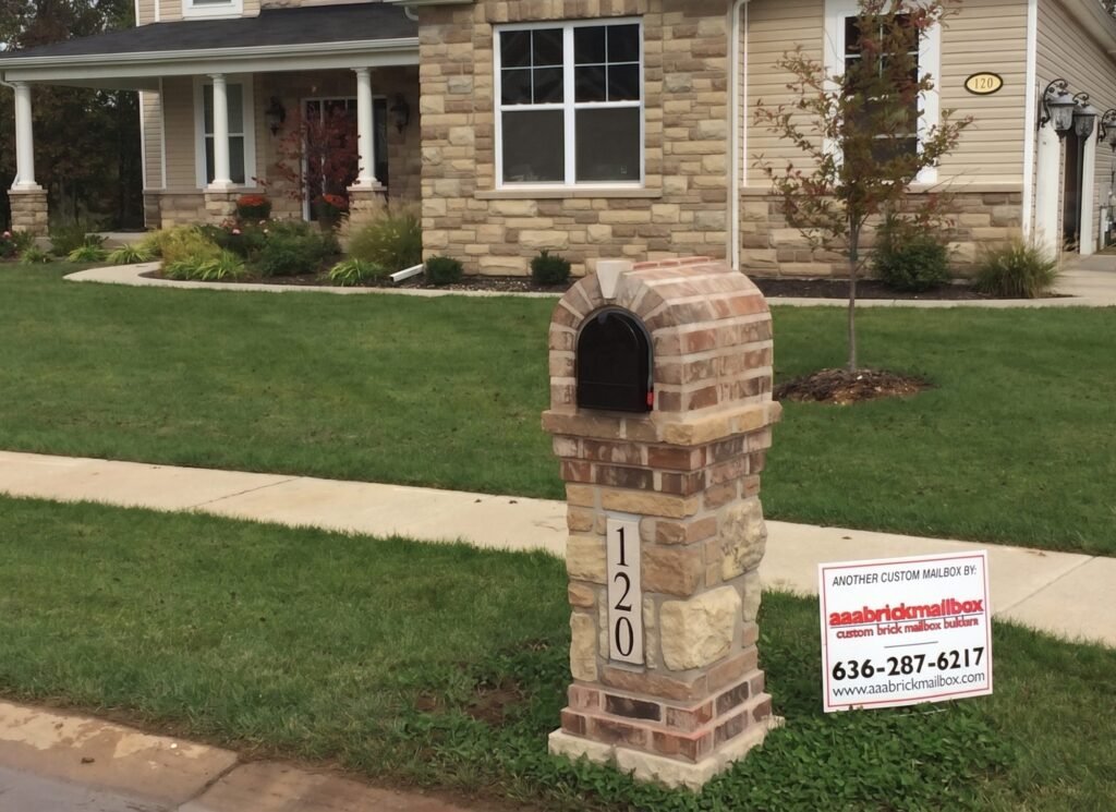 Tan and rust brick arched dome top on a stacked stone pillar with a number plate, in front of a stone-faced ranch home