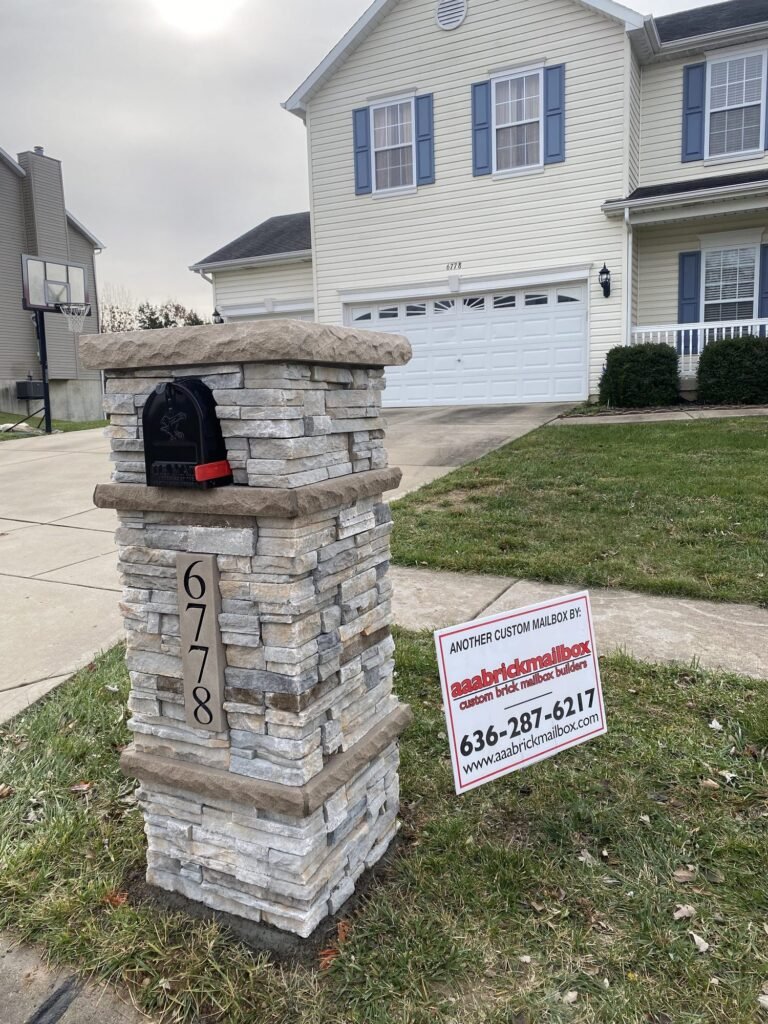 Flat stone slab cap over a light gray stacked stone pillar, no brick dome, number plate below a black mailbox, near a basketball hoop