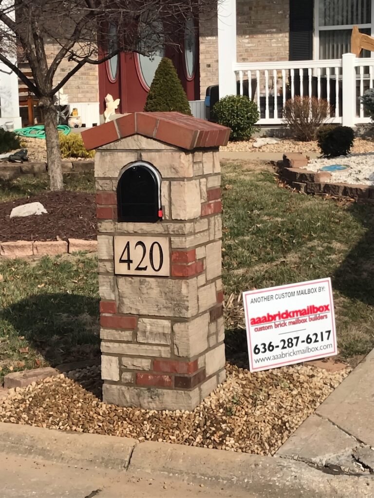 Mixed brick and stone mailbox with a peaked red brick roof and arched black door