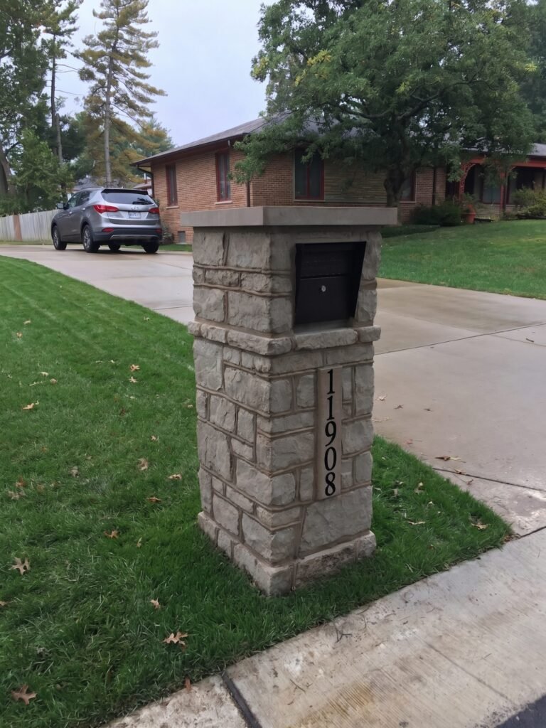 Gray stone mailbox with flat cap and front-loading door, vertical address numerals on the side face