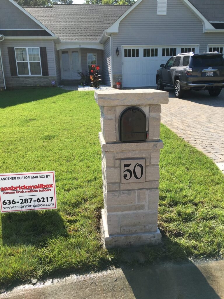 Gray stone mailbox with arched door and an engraved address plaque, brick paver driveway behind