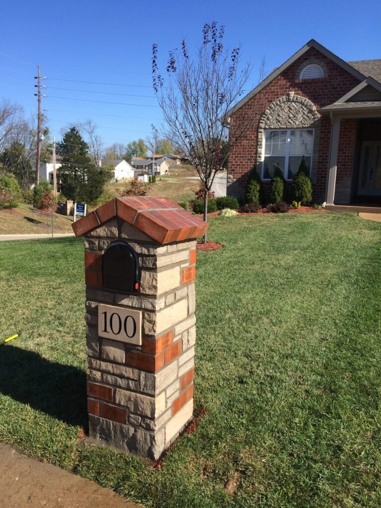 Mixed stone and brick mailbox with a peaked brick roof and arched black door