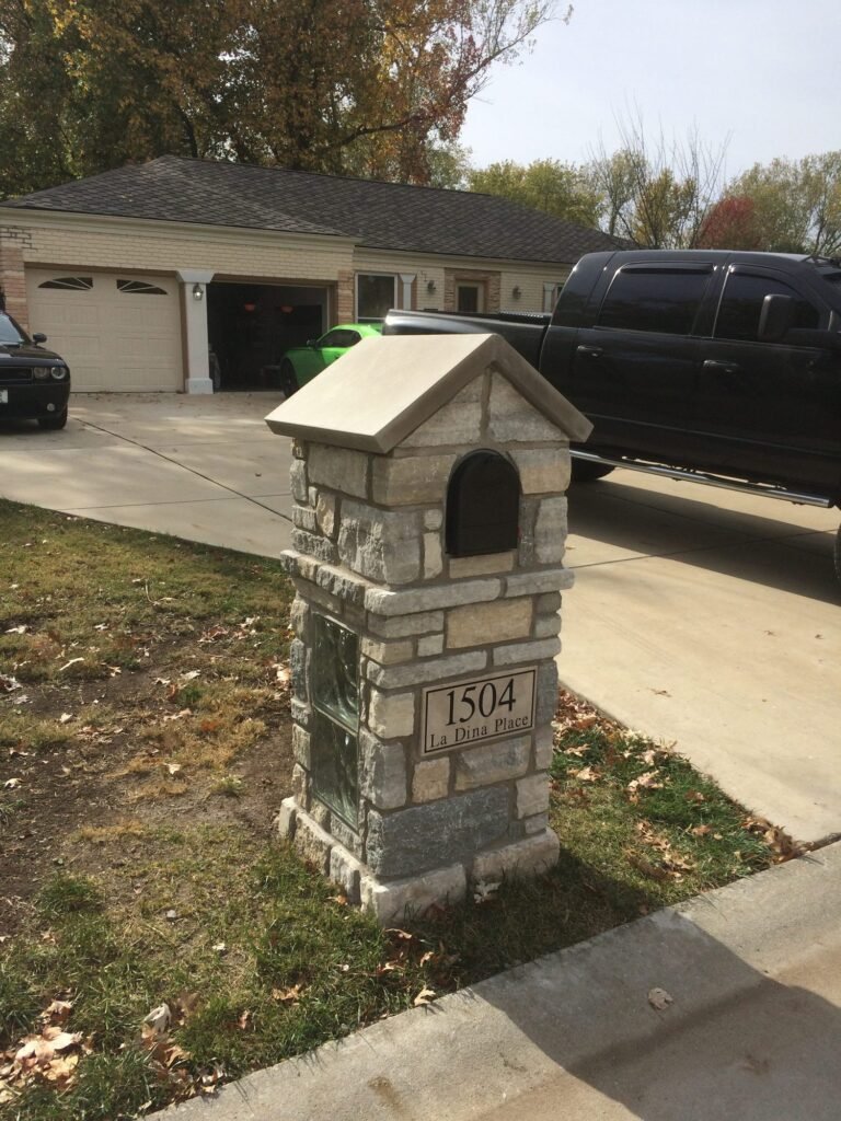 Stone mailbox with peaked cap, arched door, and a glass block accent panel built into the side