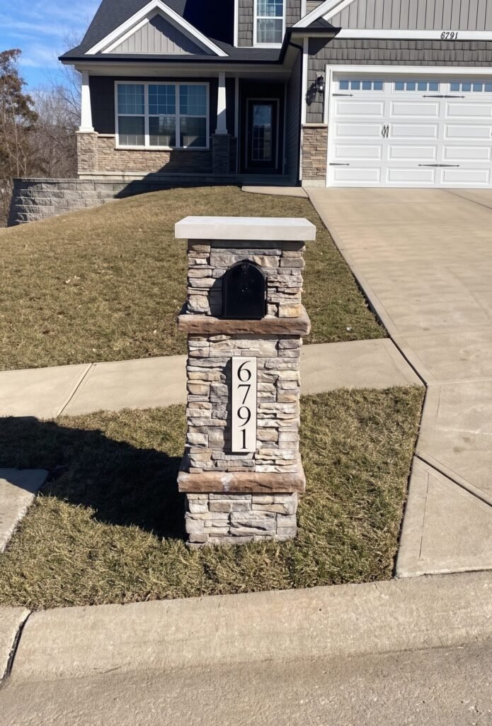 Ledge stone mailbox with contrasting brown stone accent bands and an arched black door