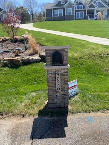 Arched stone mailbox with a peaked keystone accent, set at the foot of a curving driveway