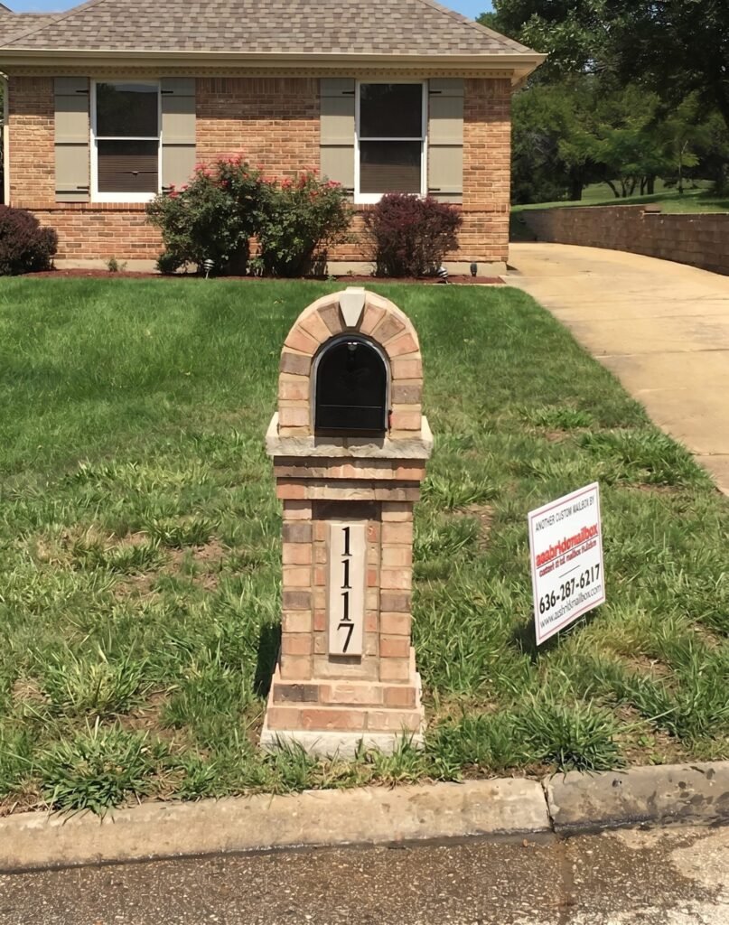 Multicolor brick mailbox with a radiating arched top and a stone base cap, rose bush blooming nearby