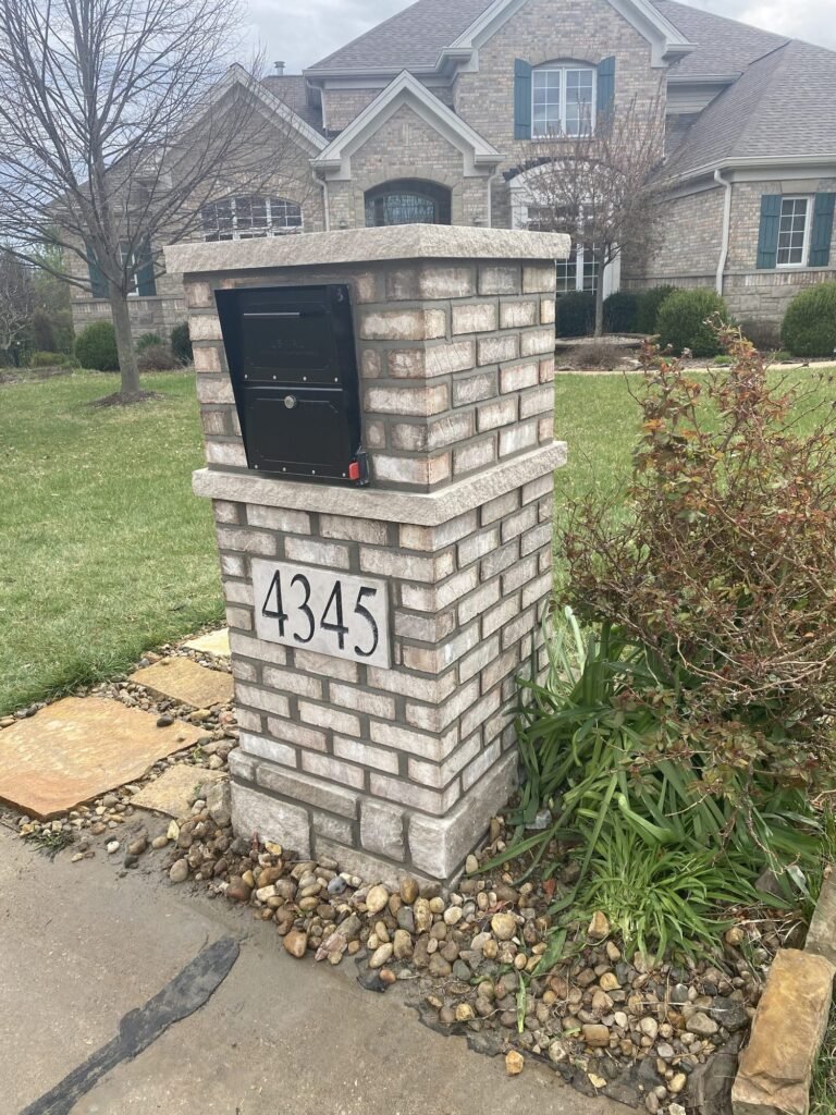 Multicolor brick mailbox with a flat stone cap, locking door shown from the side with its keyhole visible