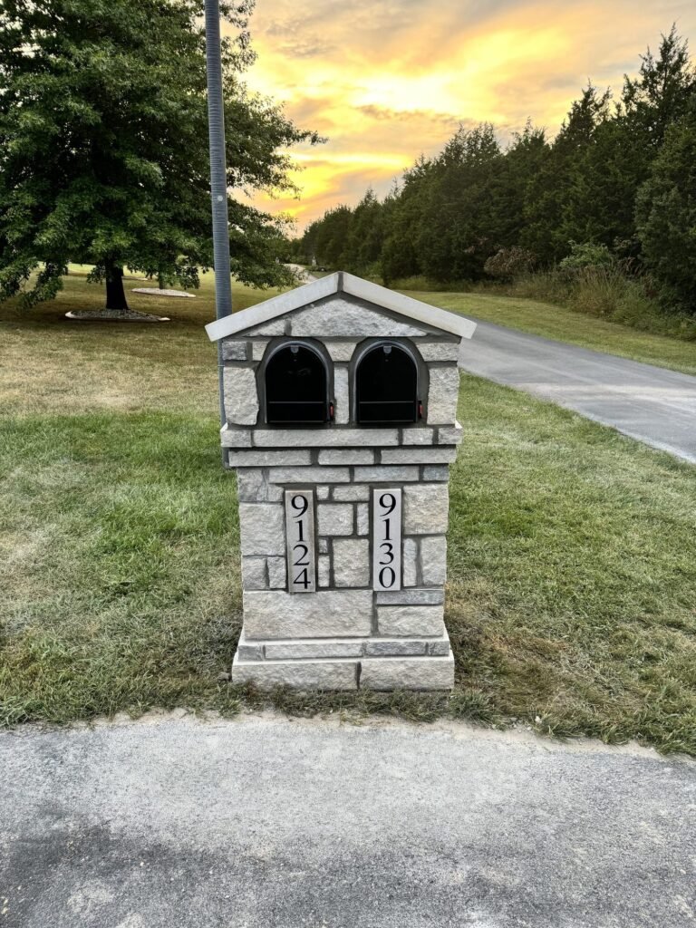 Double mailbox with a peaked stone roof and two arched doors side by side, glowing sunset sky above