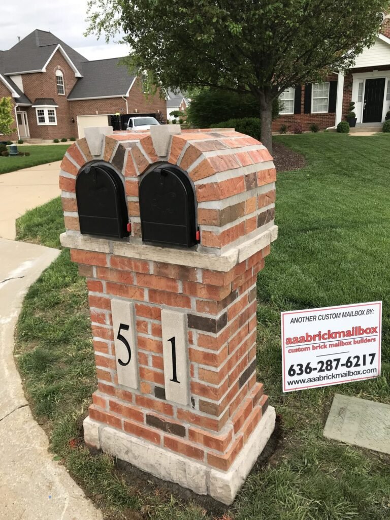 Double mailbox with two scalloped brick arches and matching stone peaks, in front of a brick two-story home