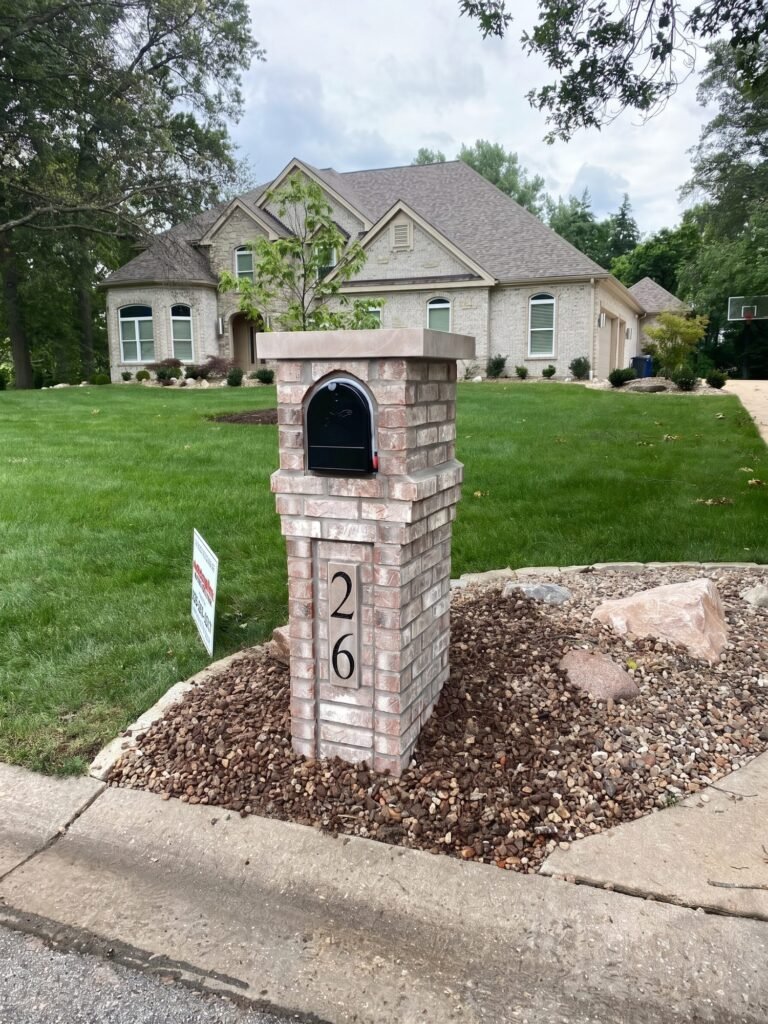 Stone mailbox with flat cap and arched brick door, set in a river rock bed with large boulders