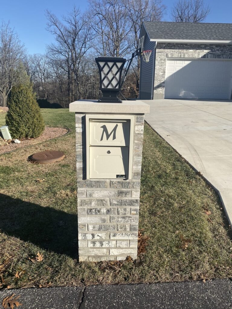 Brick mailbox topped with a black lantern light fixture, monogram initial on the cream locking door