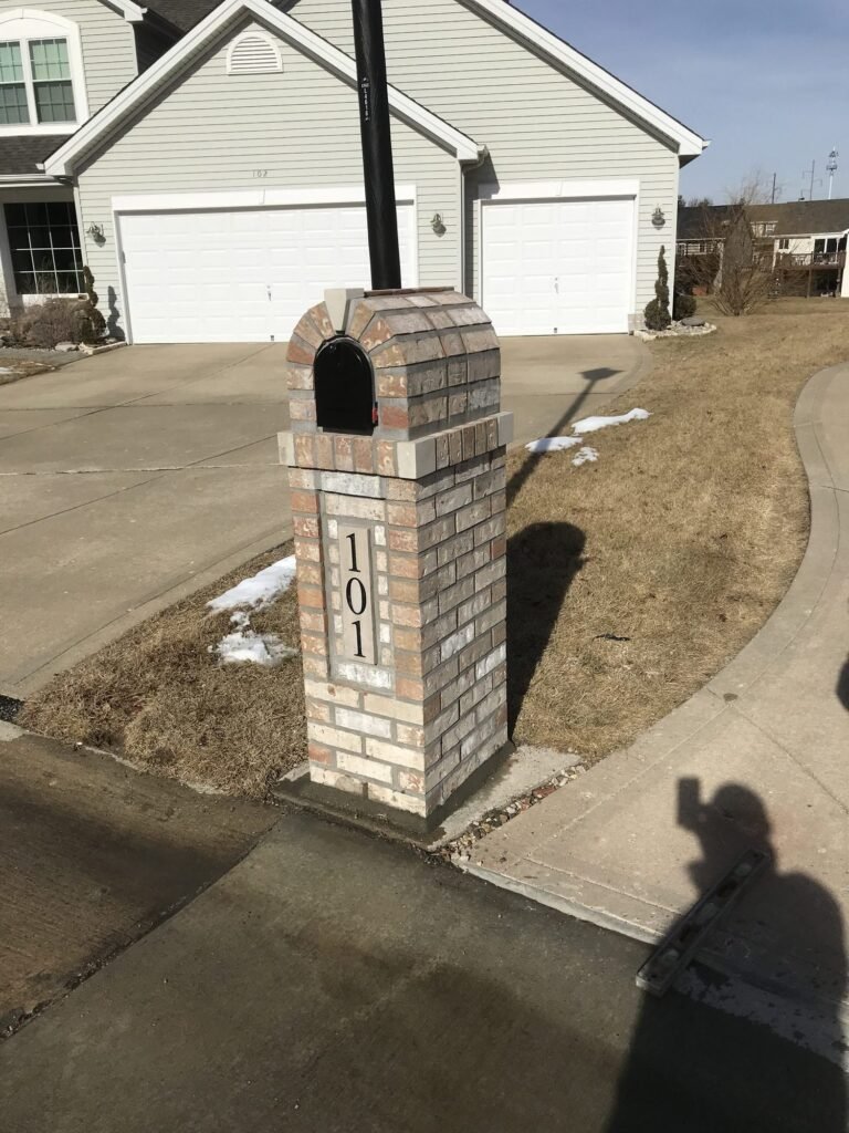 Brick mailbox with a barrel-vaulted arch top, a utility pole rising behind it, snow patches on the ground